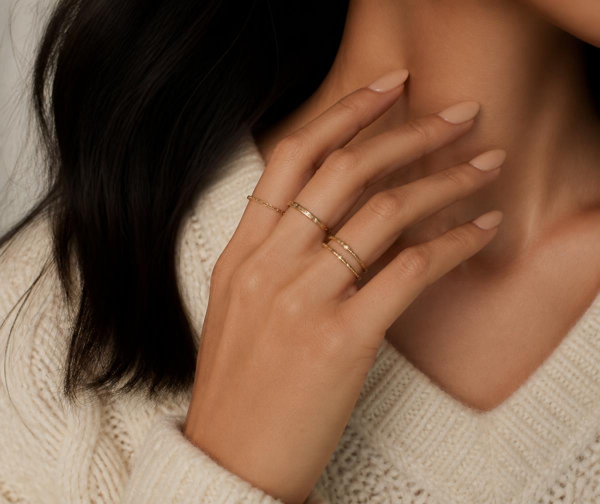 Hand with glossy nude press-on nails and gold rings resting near the shoulder