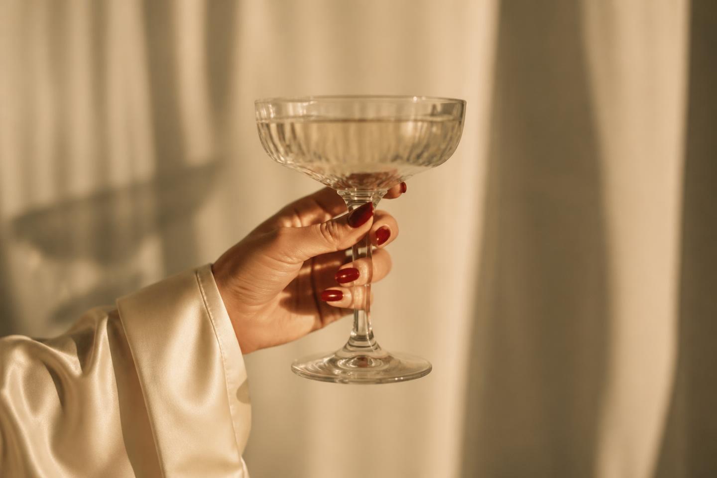 Hand with deep red press-on nails holding a coupe glass