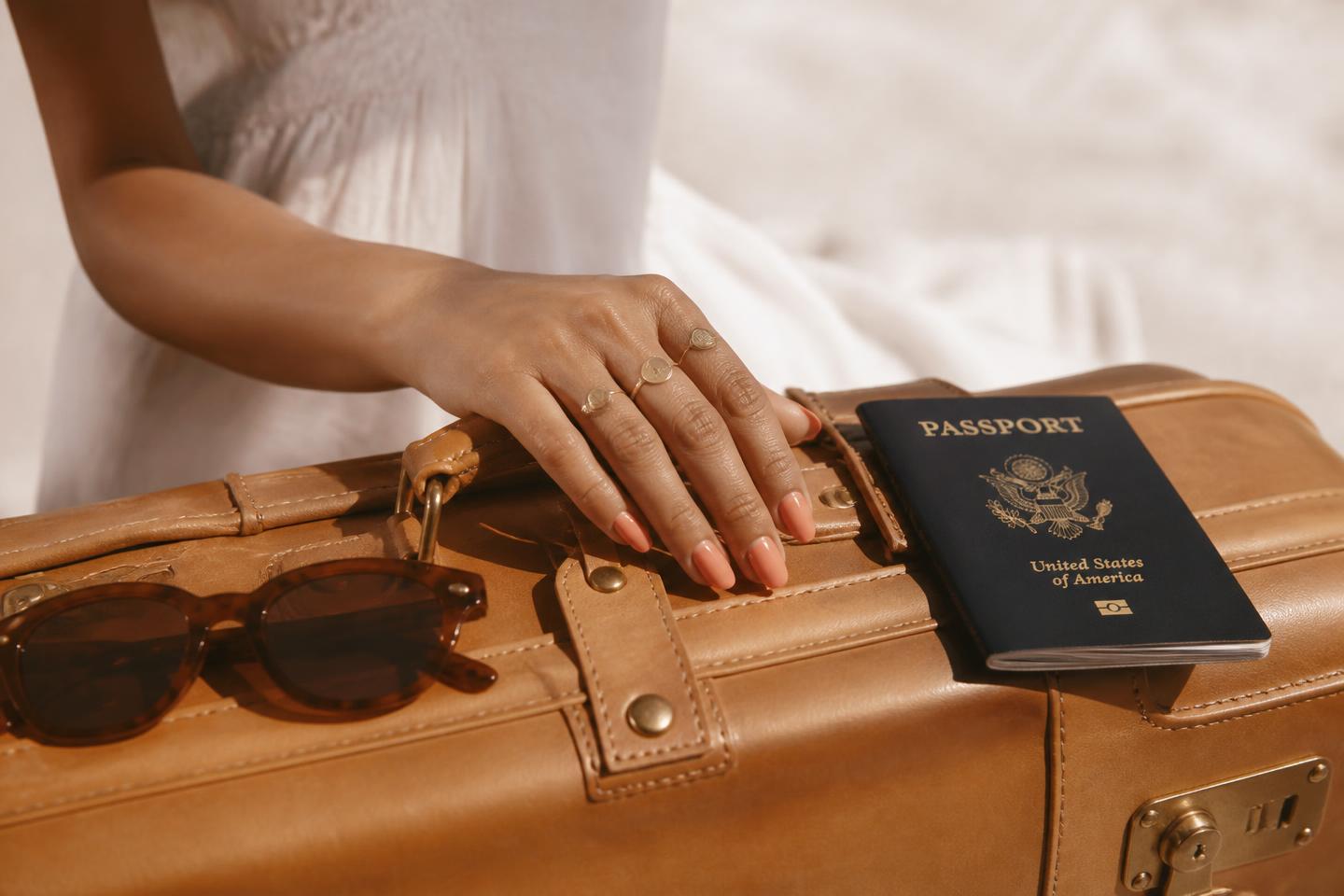 Hand with coral press-on nails resting on a tan leather suitcase